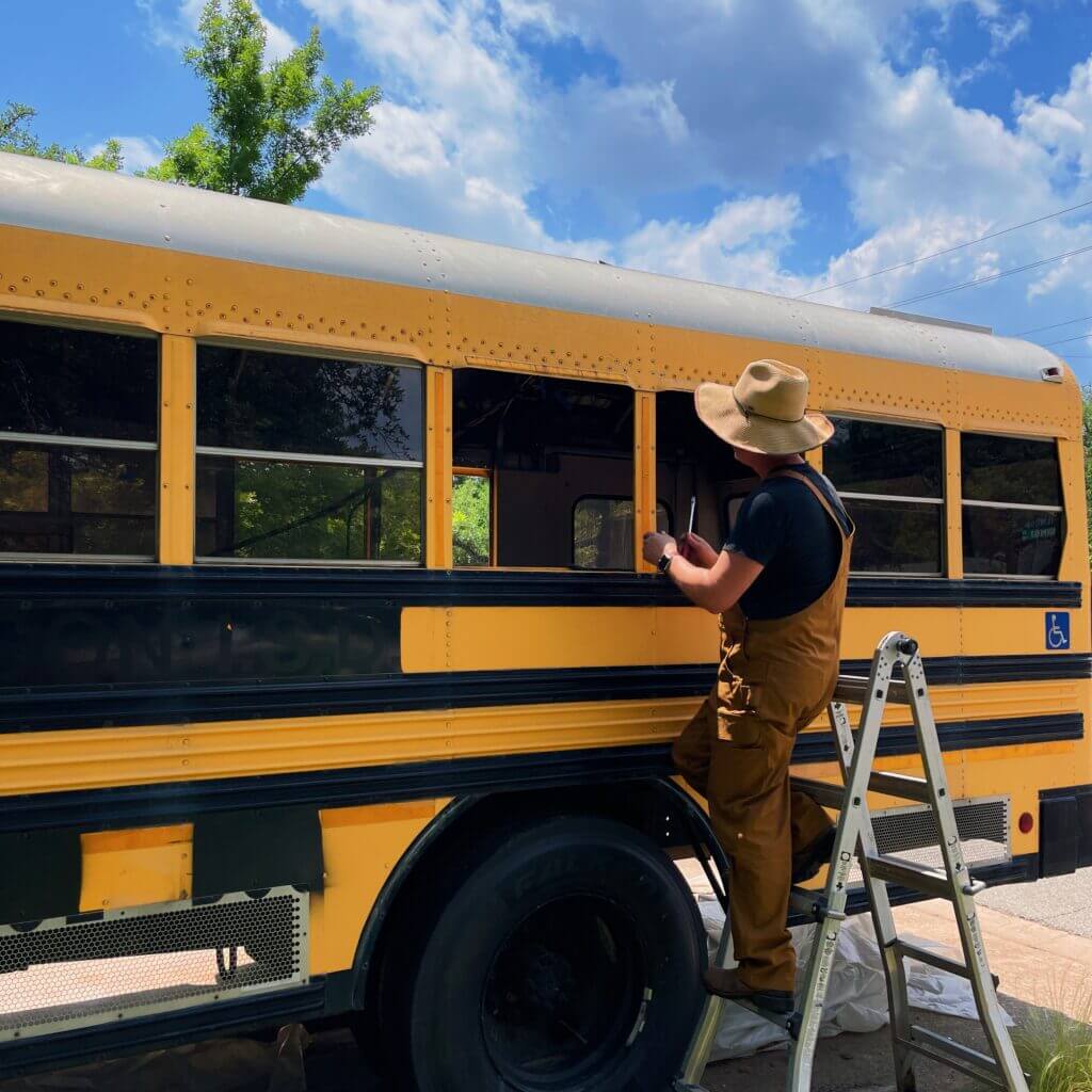 Richard works on the skoolie while wearing overalls